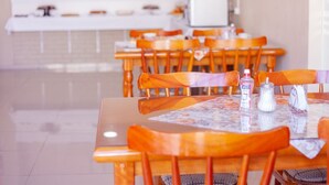 Un comedor con sillas y mesas de madera, un mostrador blanco al fondo y un dispensador de gel antibacterial sobre la mesa.