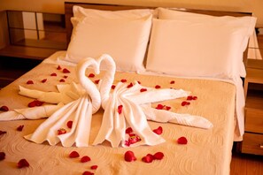 A neatly made bed with a towel arranged in the shape of a swan, surrounded by rose petals.