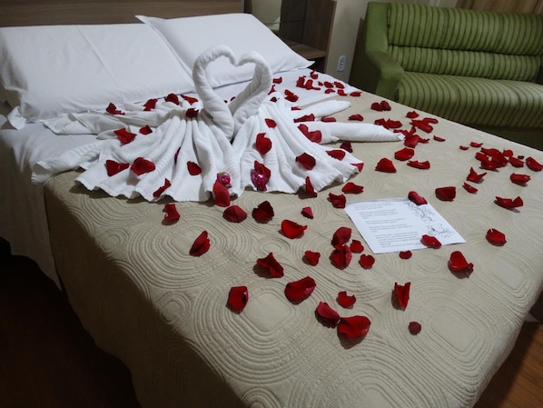 A hotel room with a bed covered in rose petals and a heart-shaped towel arrangement.