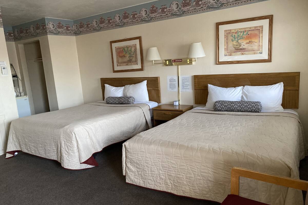 A hotel room with two beds, a nightstand with a lamp, a painting on the wall, and a carpeted floor.