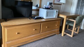 A hotel room with a wooden dresser, a flat-screen TV, a microwave, a coffee maker, and a lamp. - Rainbow Inn & Cottages (Carrizozo)
