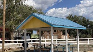 A covered picnic area with benches and a table, surrounded by a white fence. - Rainbow Inn & Cottages (Carrizozo)