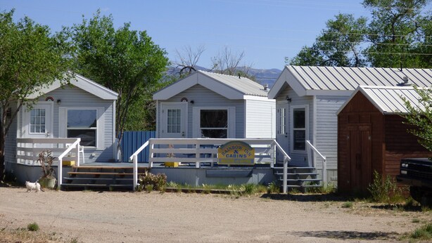 A row of cabins with a wooden staircase leading to a porch, surrounded by trees and a clear sky. - Rainbow Inn & Cottages (Carrizozo)