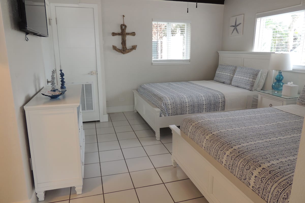 A bedroom with two beds, a dresser, a TV, and a window with blinds.
