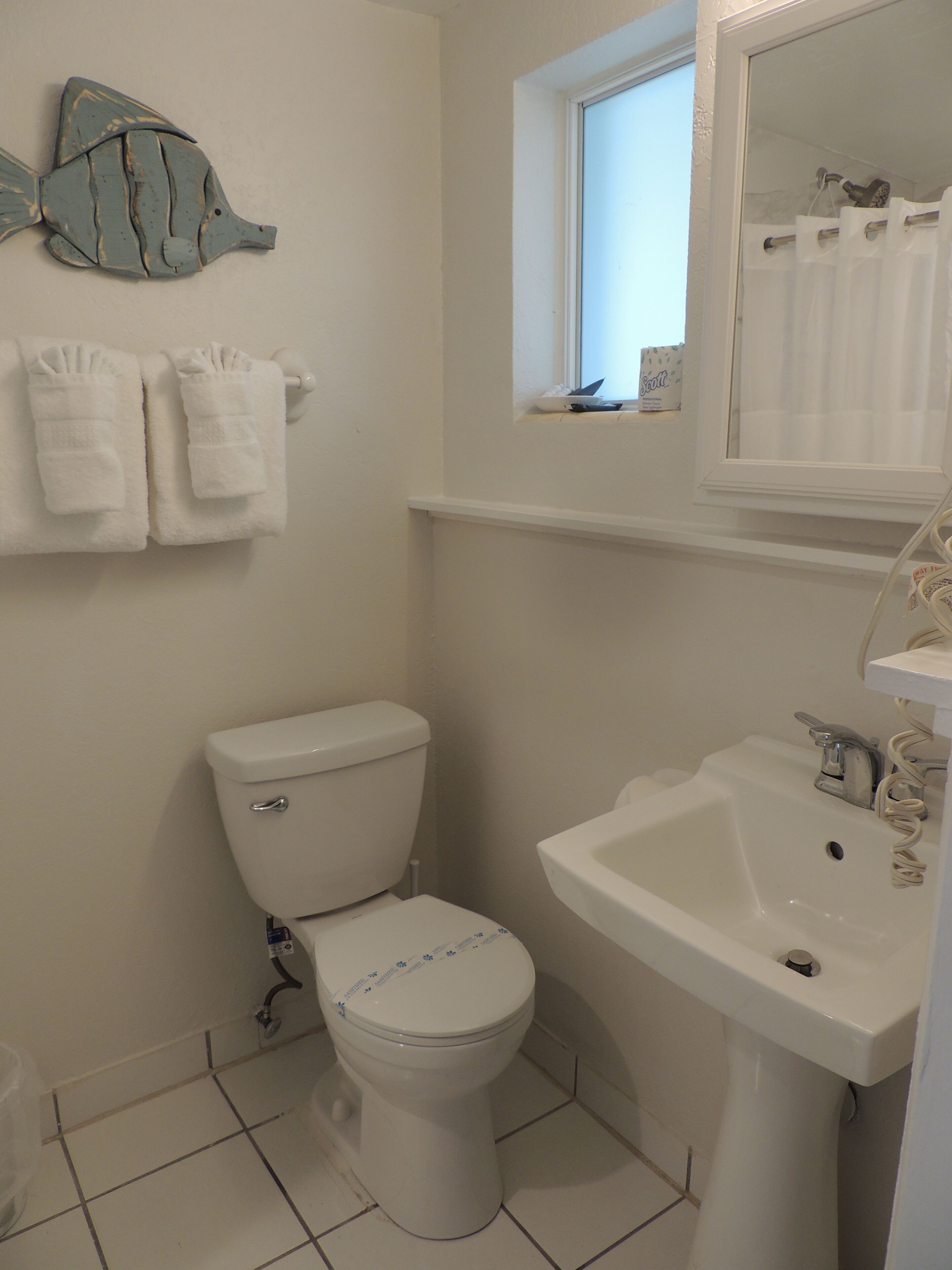 A bathroom with a toilet, sink, and a window above the sink.