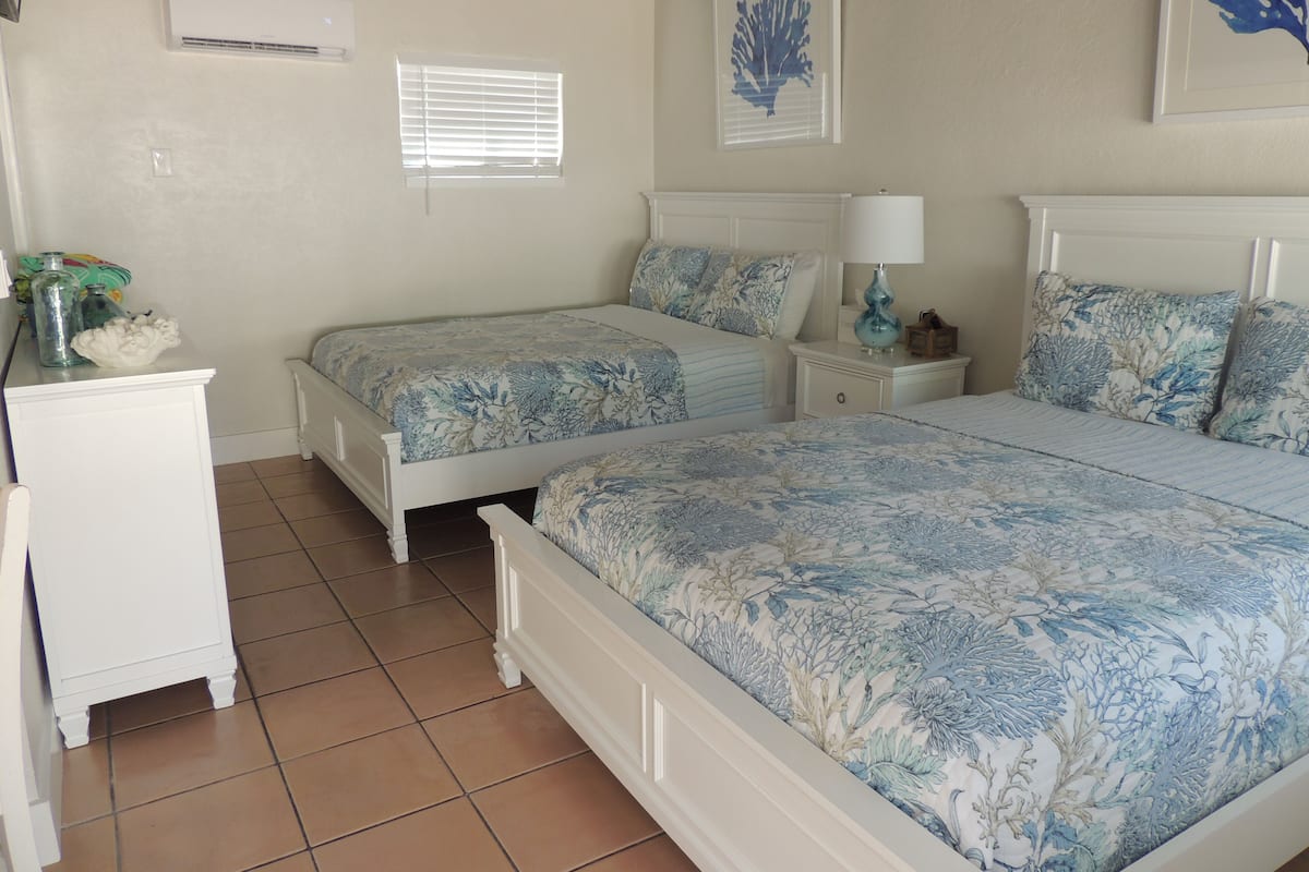 A bedroom with two beds, a nightstand, a dresser, and a window with blinds.