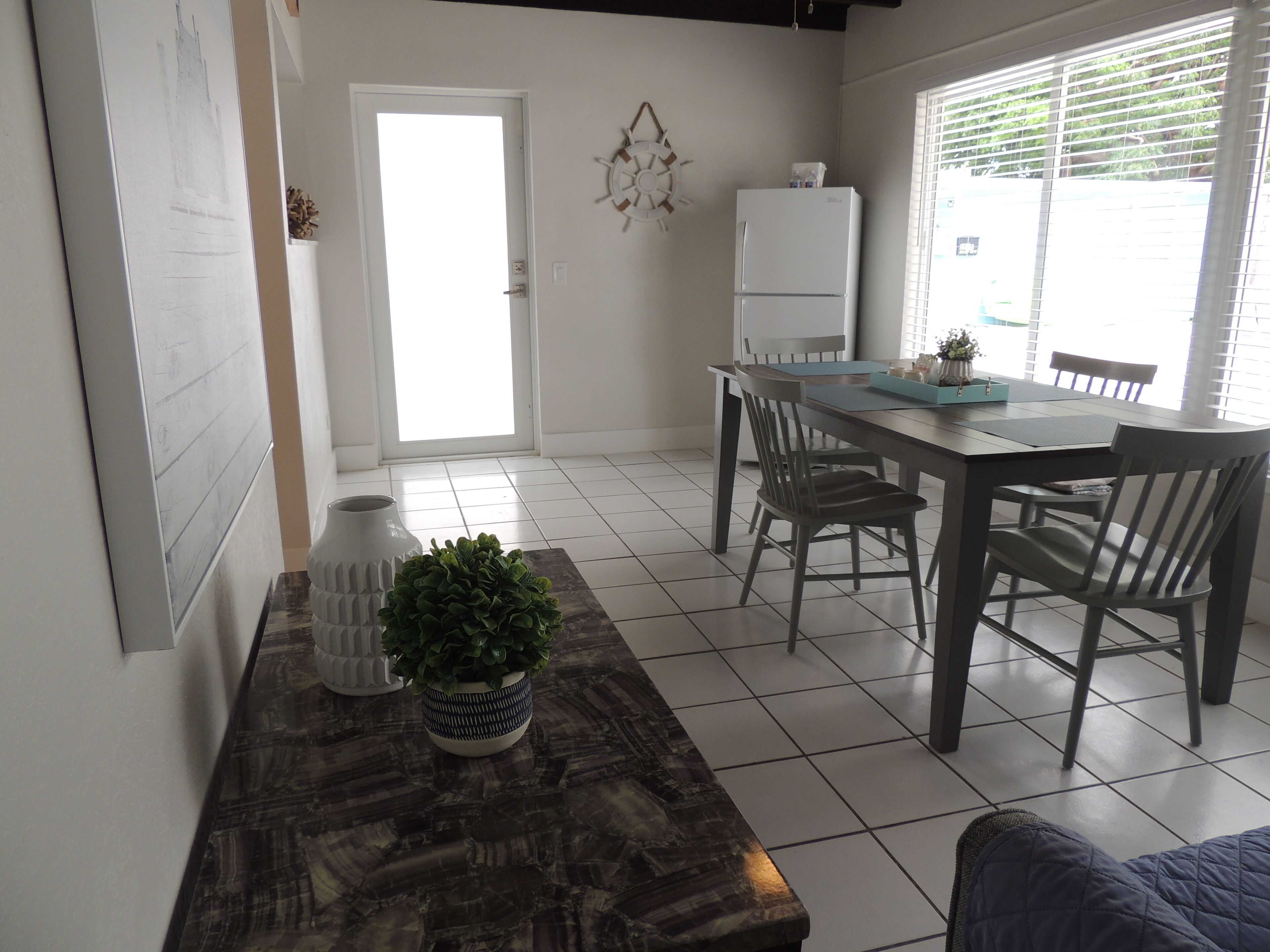A dining area with a wooden table, chairs, a white refrigerator, and a potted plant.