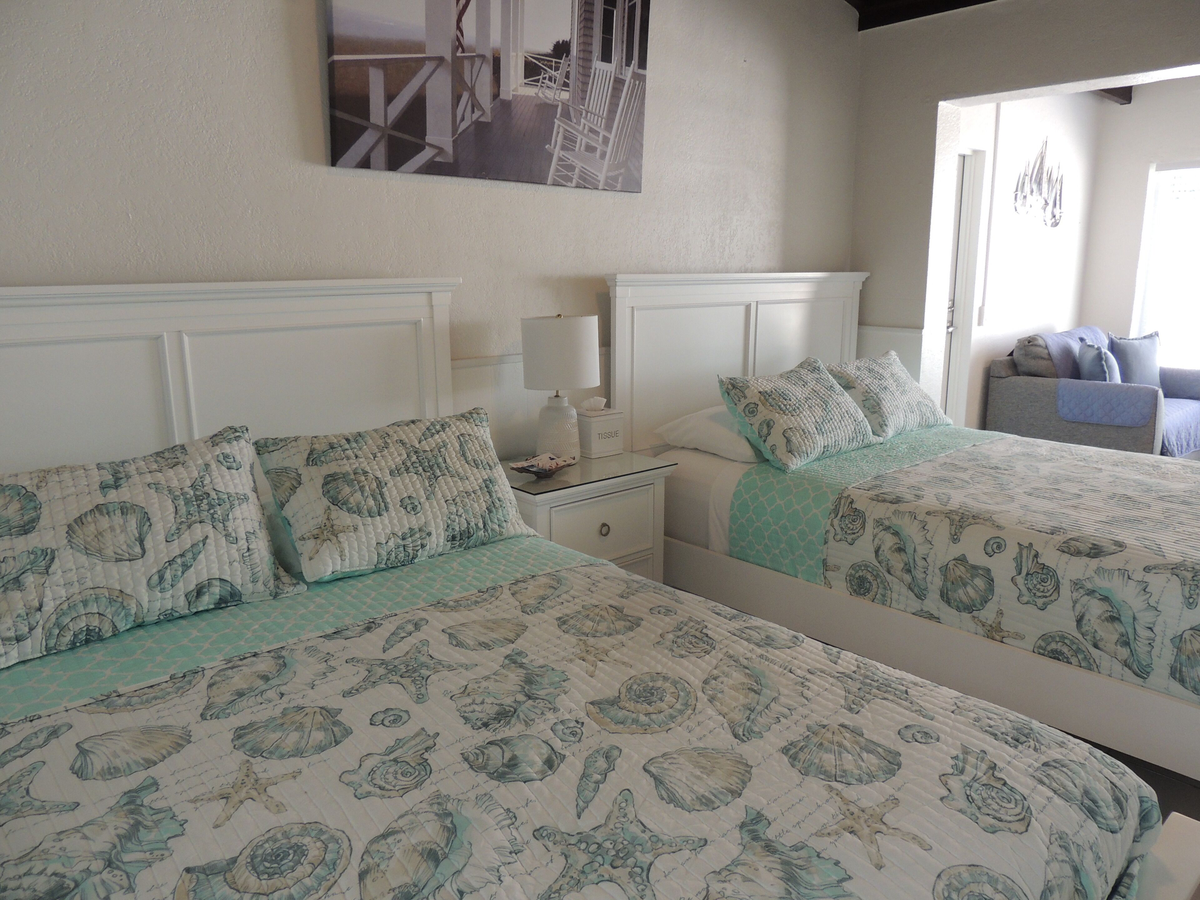 Une chambre avec deux lits, chacun doté d’une tête de lit matelassée et d’oreillers assortis. On y trouve une table de chevet avec une lampe et une boîte à mouchoirs.