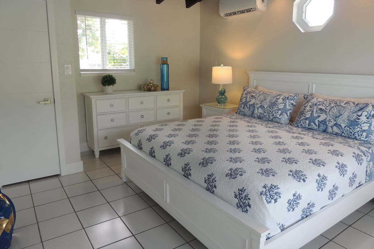 A bedroom with a bed, a nightstand, a dresser, a window, and an air conditioning unit.