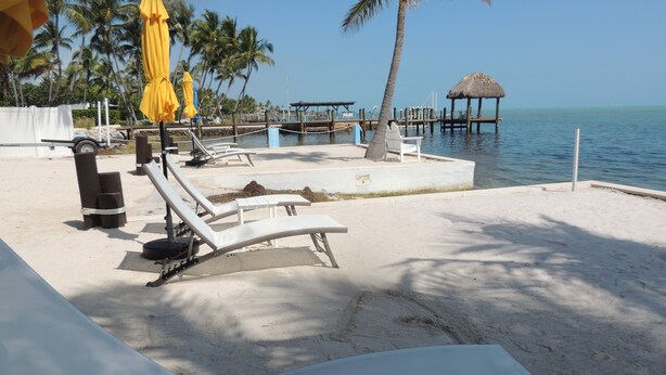 A beachside lounge area with sun loungers, a thatched structure, and a view of the ocean. - Sands of Islamorada (Islamorada)