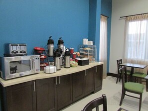 A kitchenette with a microwave, toaster, coffee makers, and a glass display case with food items.