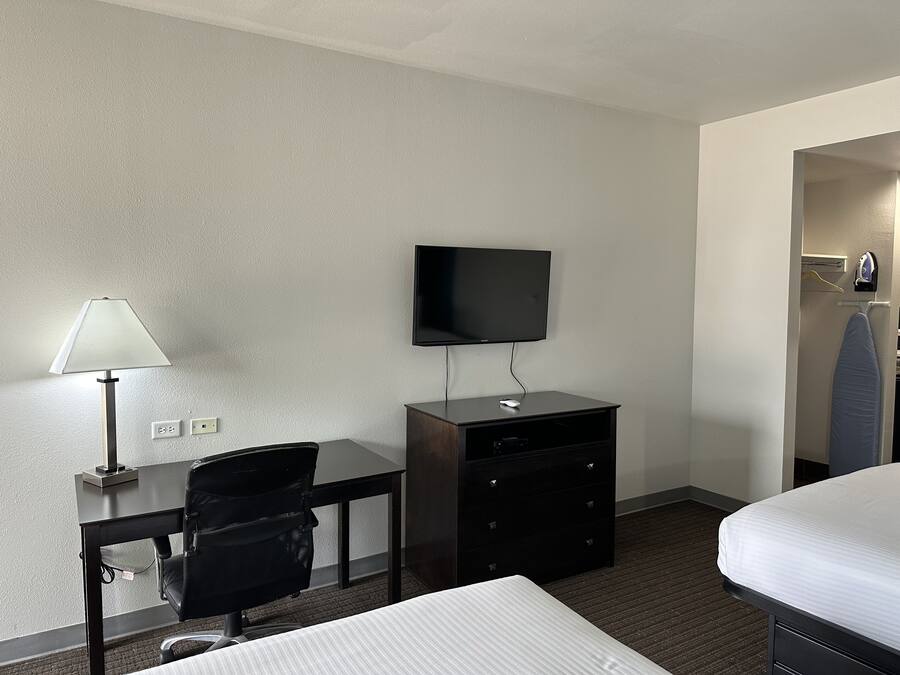 A hotel room with a bed, a desk with a chair, a television, and a dresser.