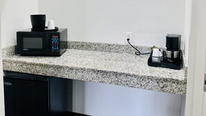 Una cocina con encimera de granito, microondas, cafetera y lavavajillas.