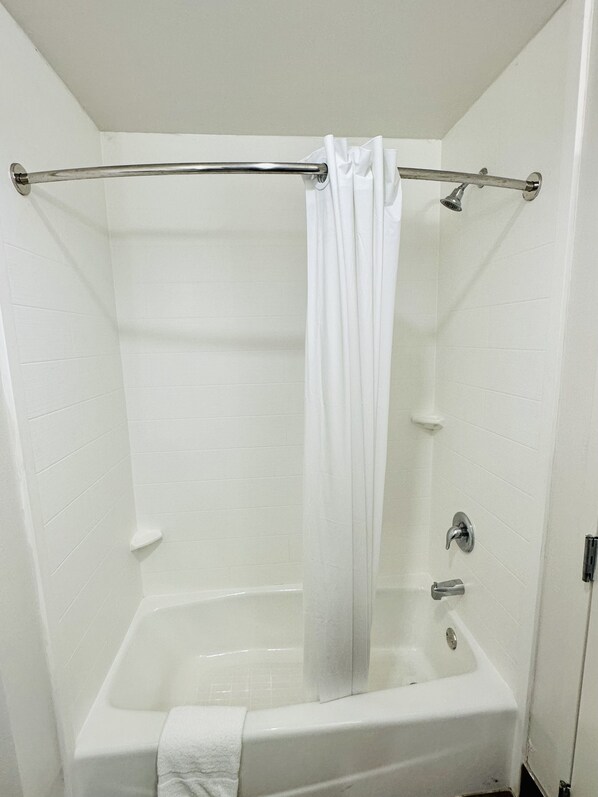 A white bathtub with a shower curtain rod and a towel hanging on the side.