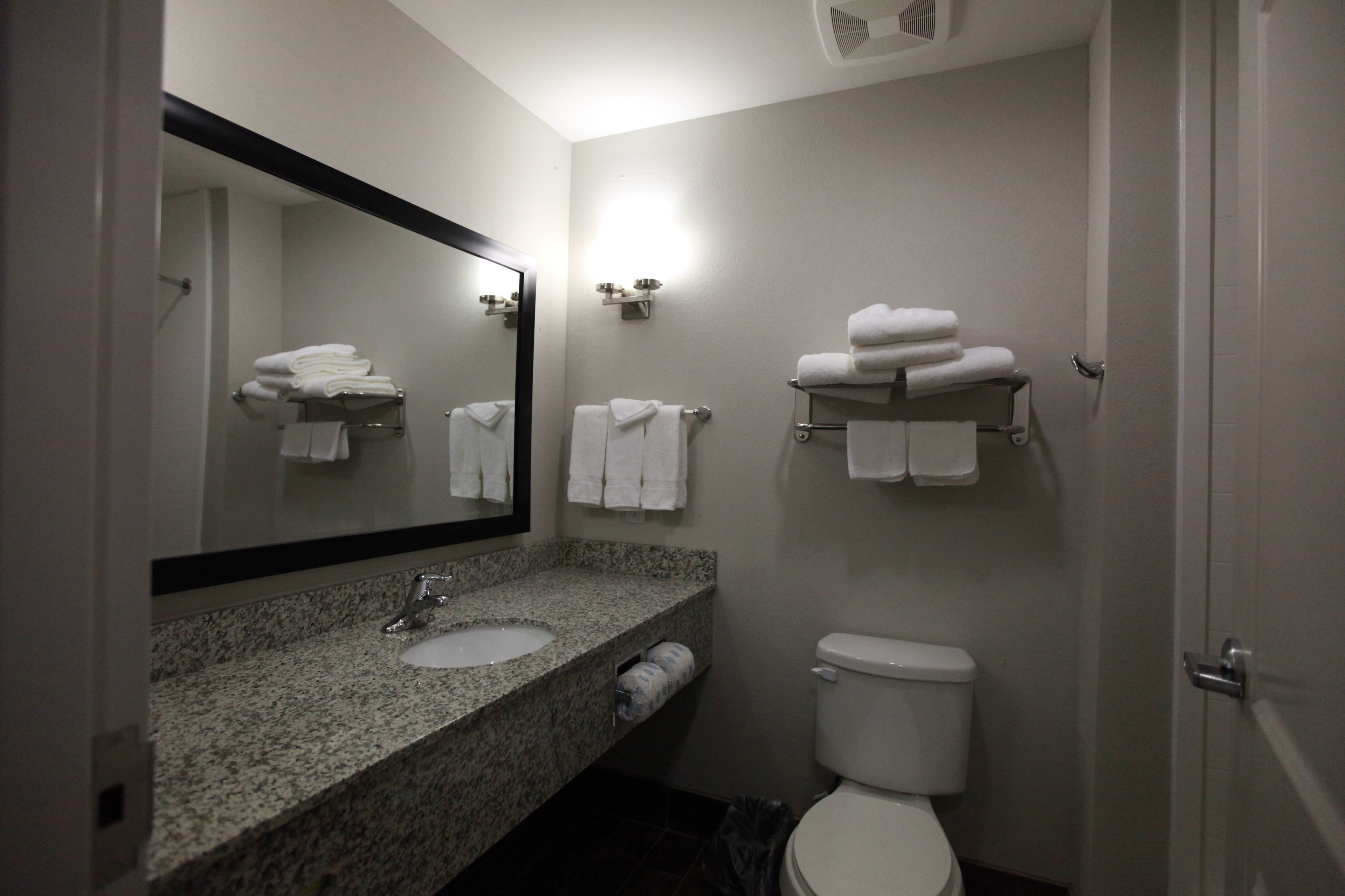 Een badkamer met een granieten wastafel, een toilet en een spiegel. Handdoeken liggen op een rek en er is een plankje.