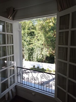 Una ventana abierta con barandilla de metal, con vistas a un espacio exterior verde y frondoso.