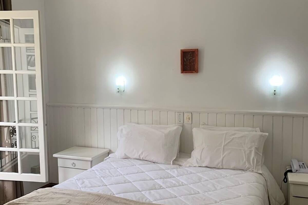 Quarto com cama, mesas de cabeceira, luminária de parede e ventoinha no teto.