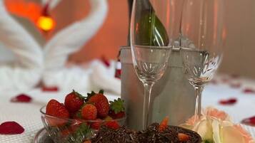 Ein Tisch mit einer Schale Erdbeeren, Schokoladenraspeln und einer Rose. Zwei Gläser und eine Champagnerflasche sind ebenfalls vorhanden.