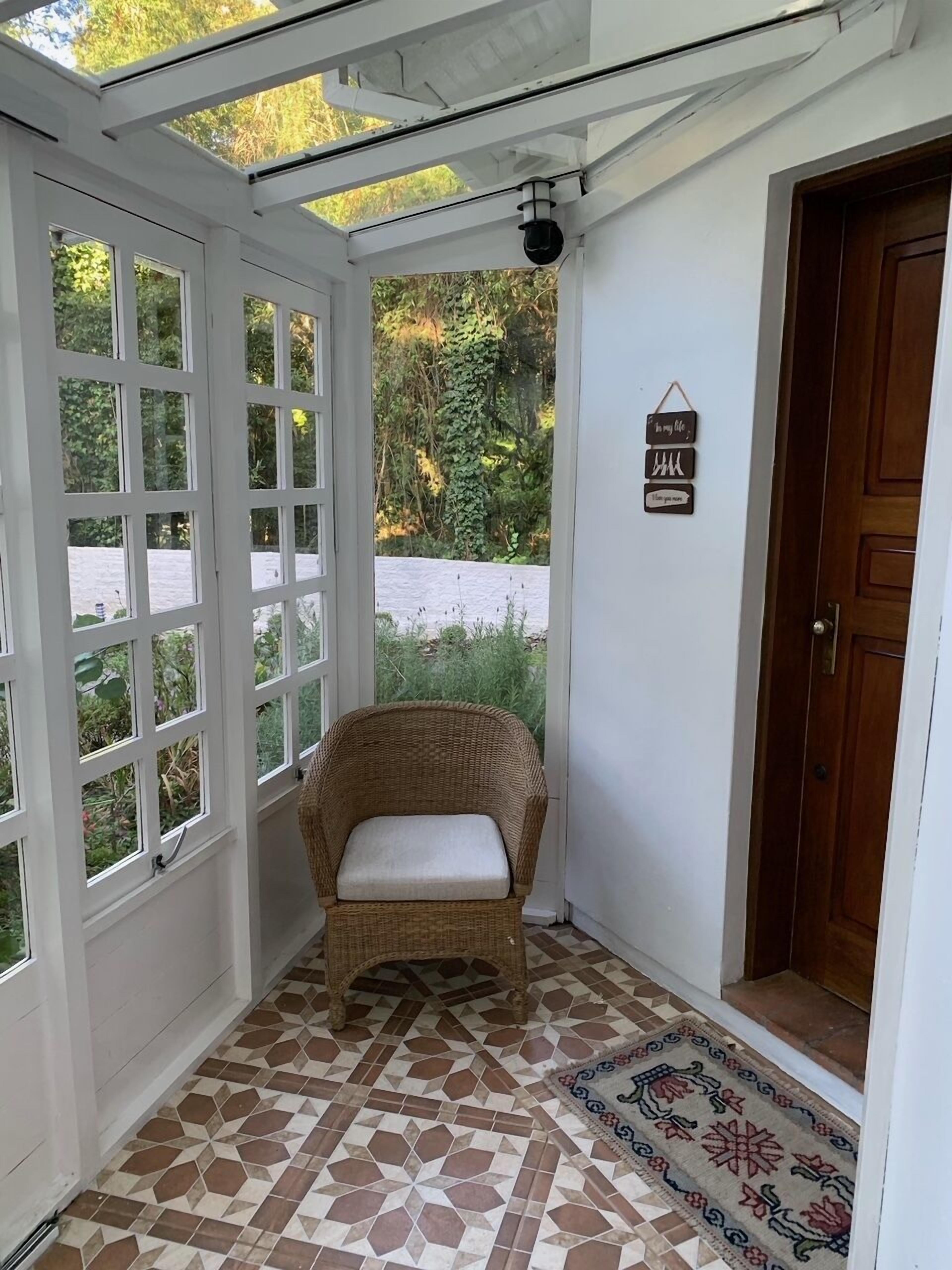 Una habitación con una silla de mimbre, un tapete estampado y una puerta de madera.