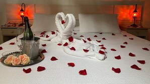 Habitación de hotel con una cama bien hecha, pétalos de rosa, una botella de champán y dos lámparas encendidas.
