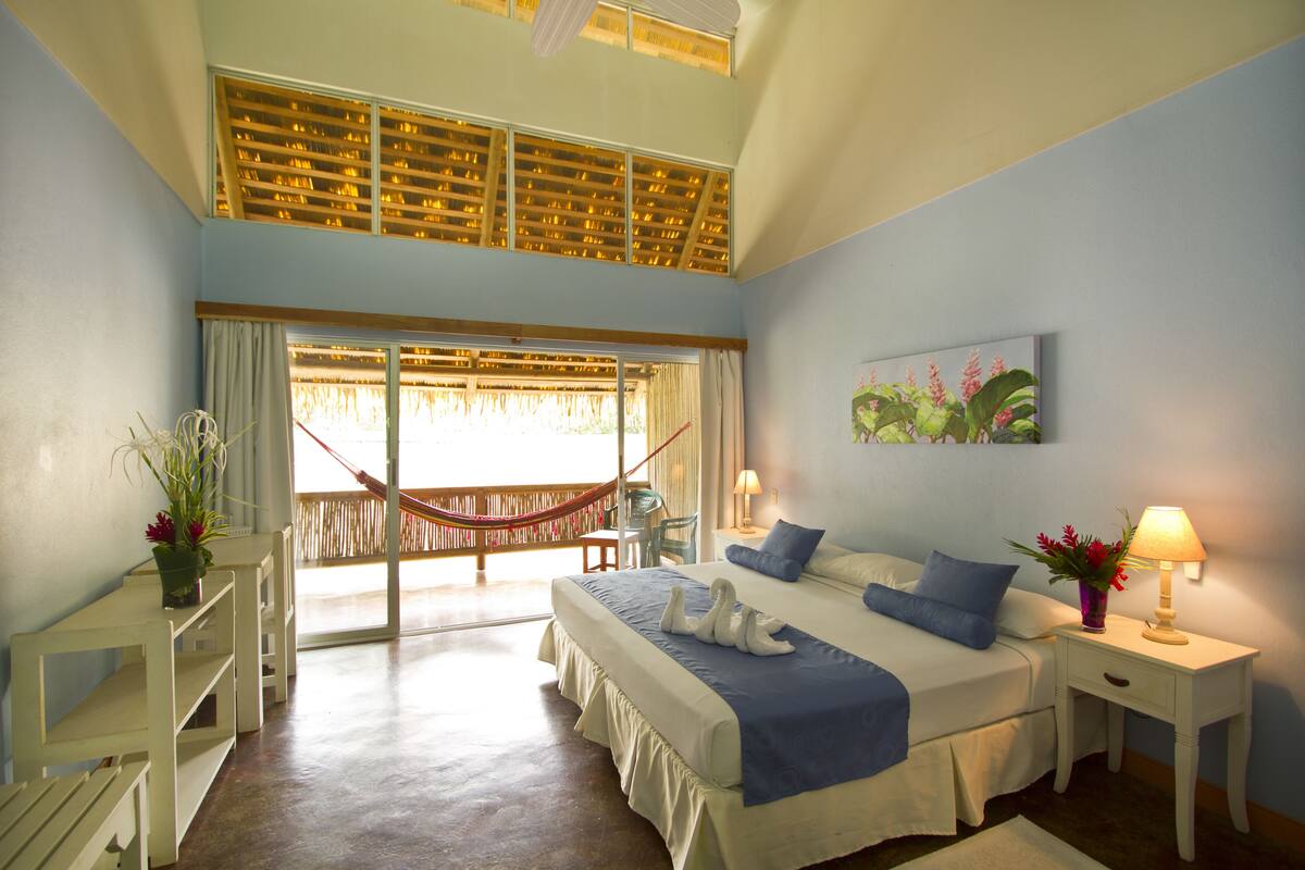 A bedroom with a bed, nightstands, a desk, a hammock, and a window with curtains.