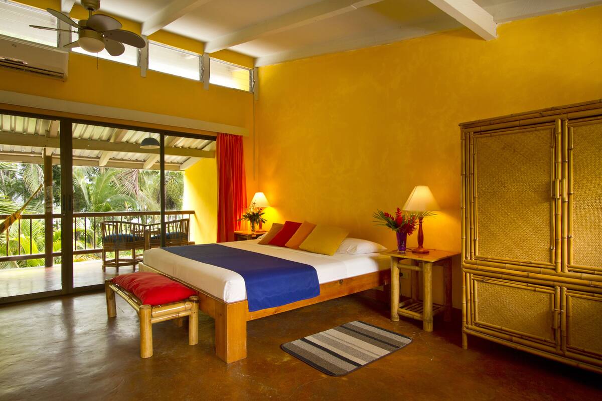 A room with a bed, a wooden bench, a nightstand, and a large window.