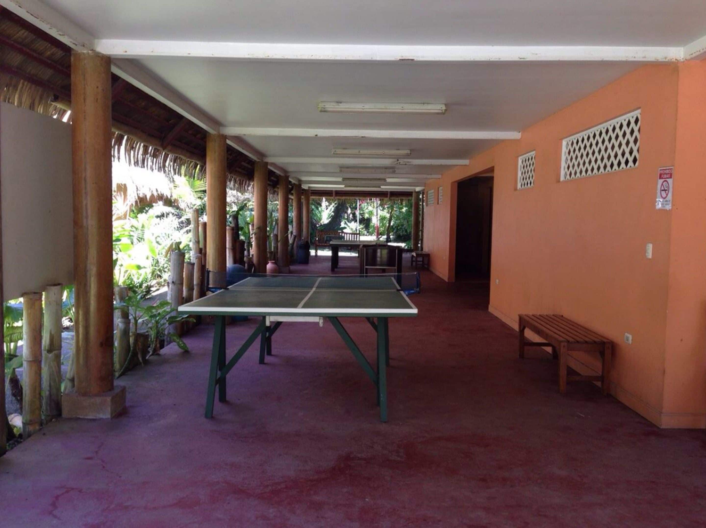 Un espacio al aire libre techado con mesa de ping pong, bancos y una estructura de techo de paja.
