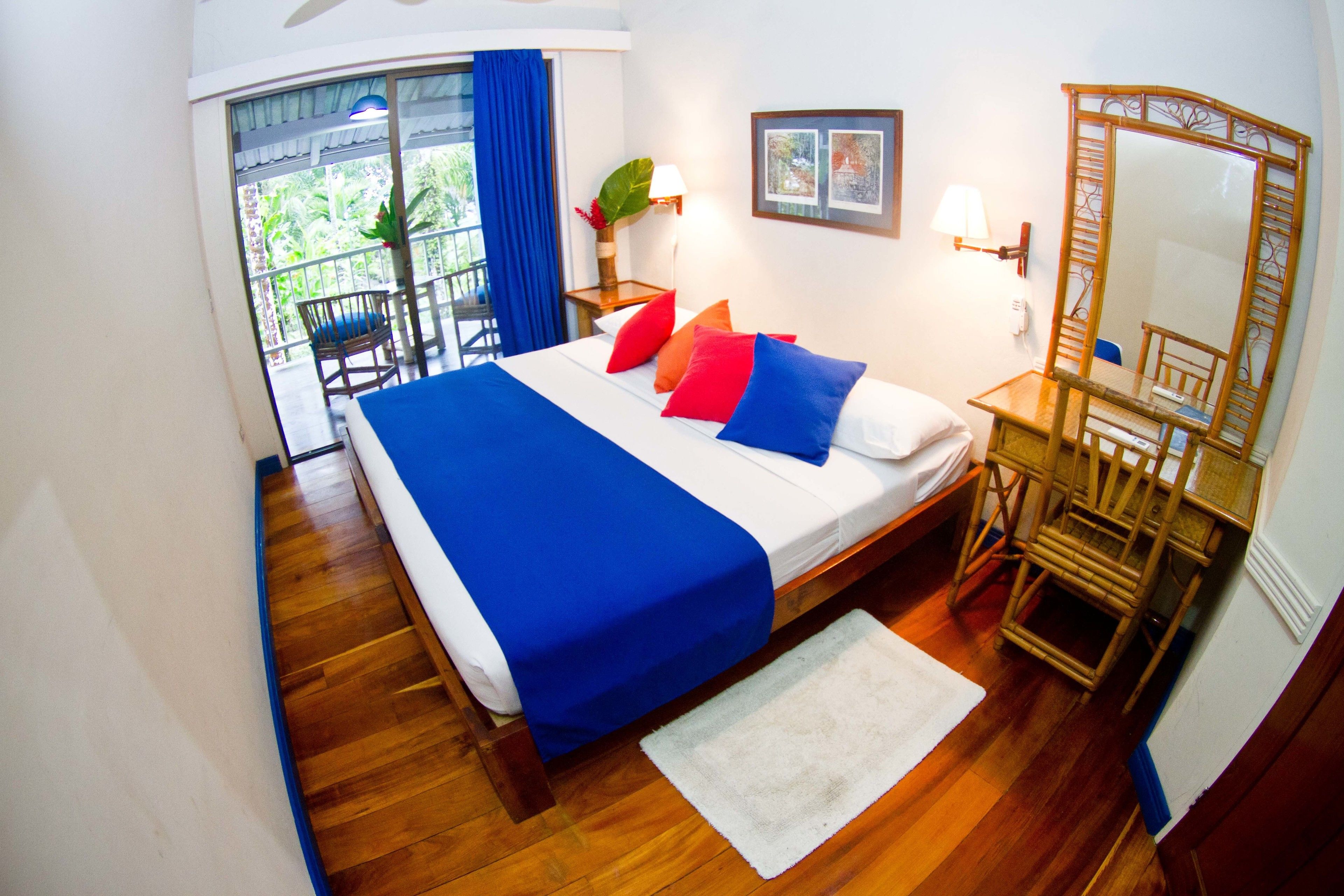 Une chambre avec un grand lit, un balcon avec une chaise, un plancher en bois et un miroir.