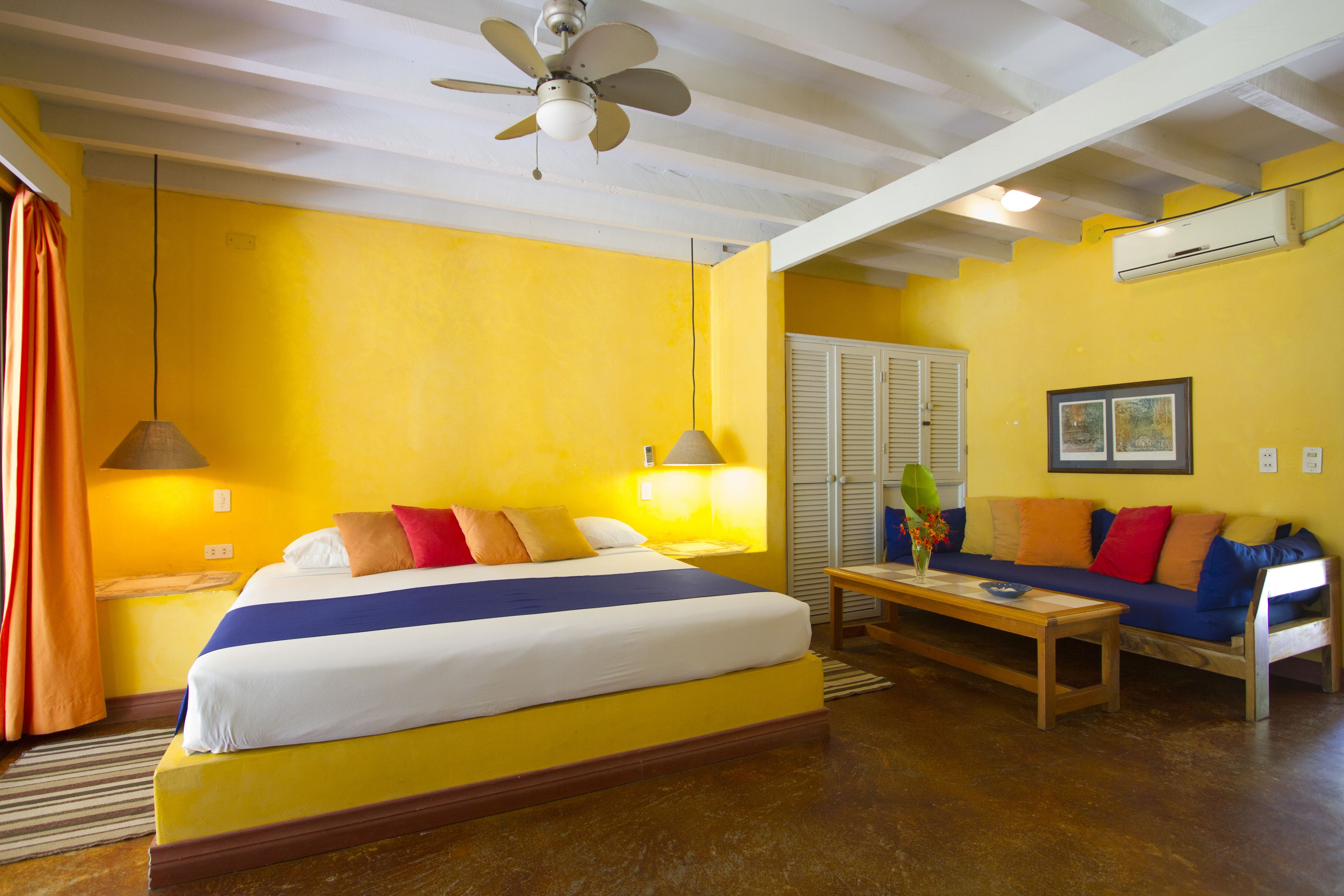A hotel room with a large bed, a sofa, a table, and a ceiling fan.