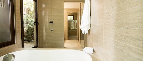 Une salle de bain moderne dotée d’une grande baignoire, d’une douche à parois de verre et offrant une vue sur un jardin grâce à une porte ouverte.