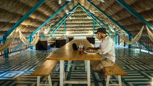 A dining area with a wooden table, benches, and a thatched roof. - Jungle Lodge Hotel (Flores)