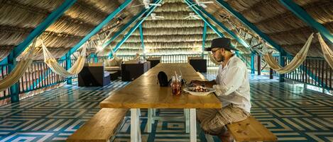 A dining area with a wooden table, benches, and a thatched roof.