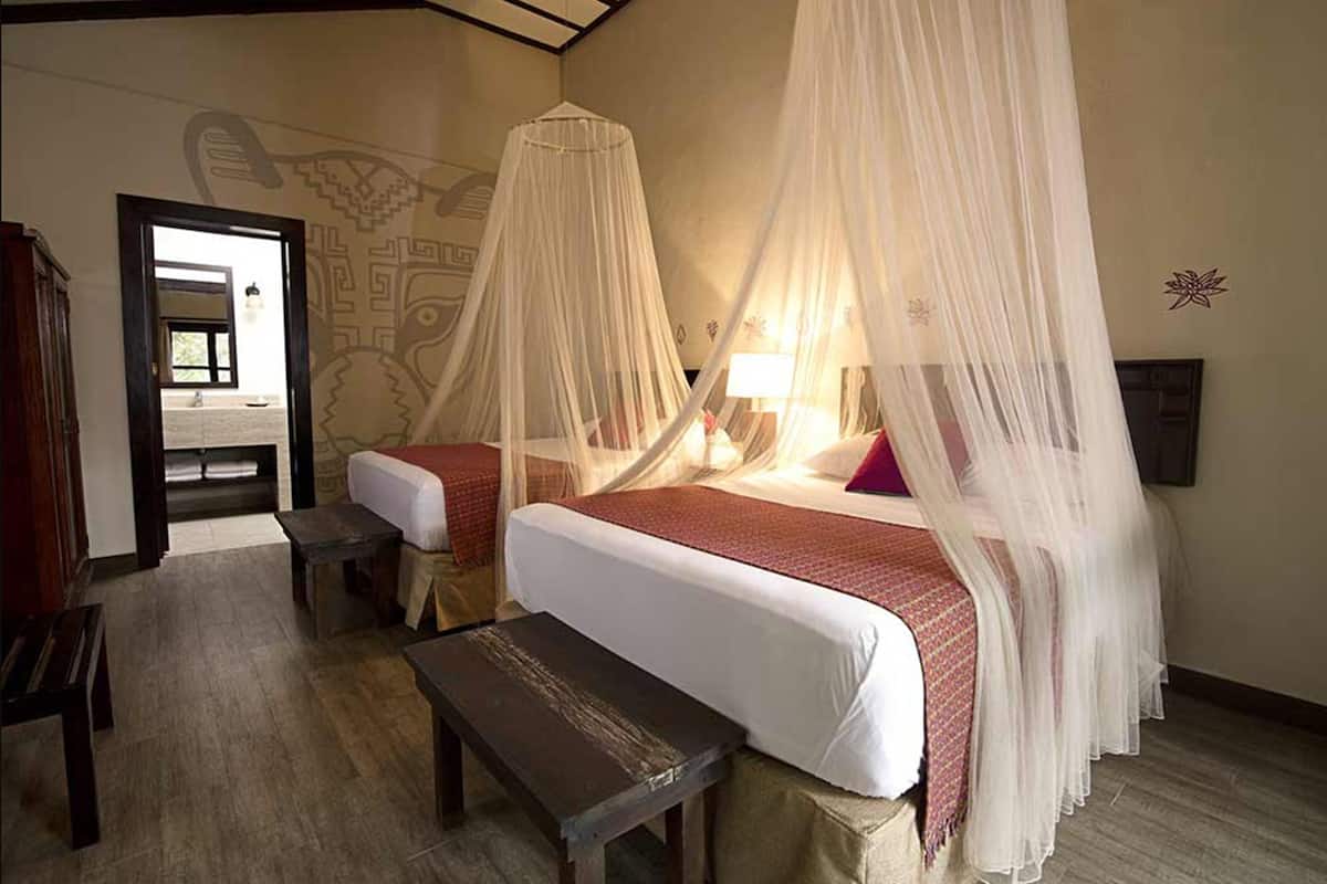 A room with two beds, each with a canopy, a bench, and a wall mural.