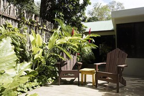 A patio area with two wooden Adirondack chairs, a small wooden table, and lush tropical plants. - Jungle Lodge Hotel (Flores)