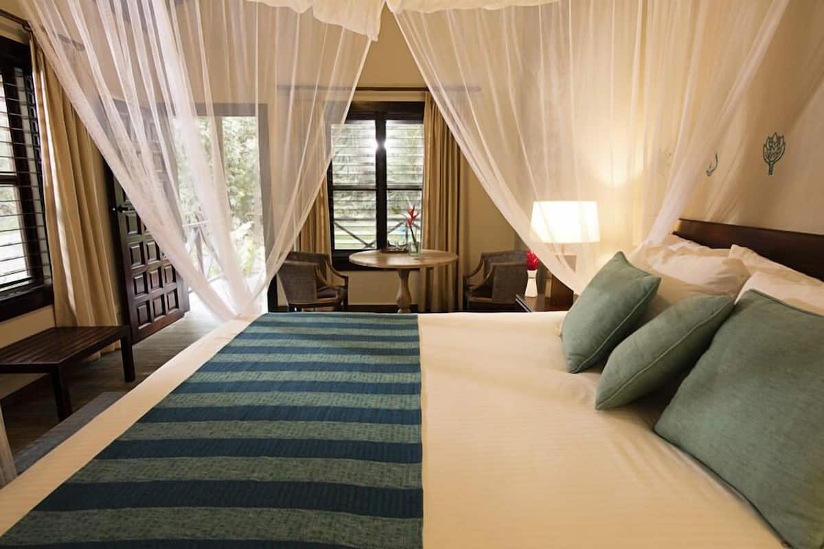 A hotel room with a bed, a bedside table, a chair, a small table, and a window with curtains.