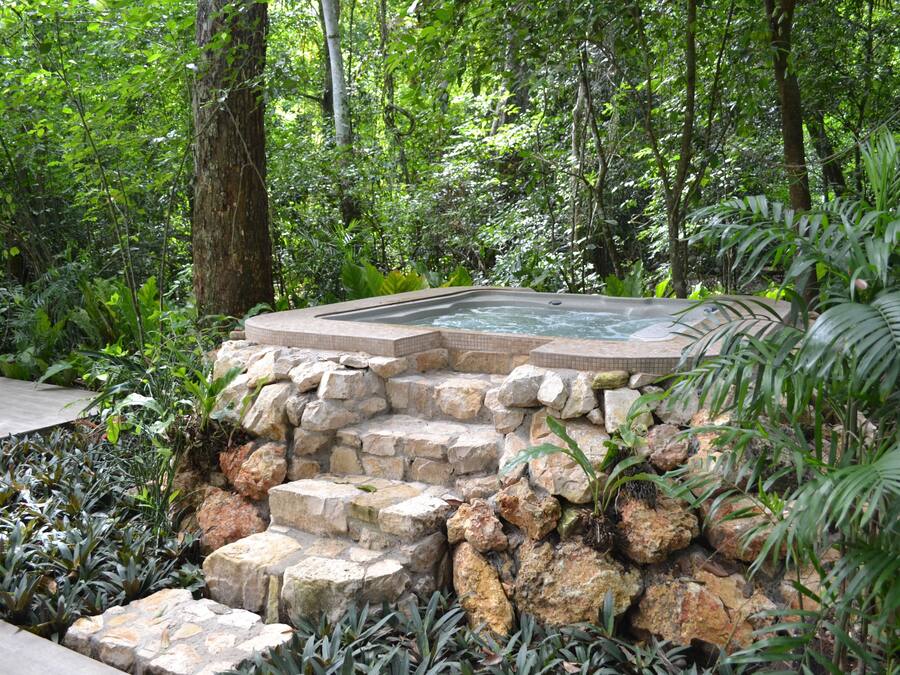 Uma banheira de hidromassagem rodeada por um muro de pedra e vegetação exuberante.