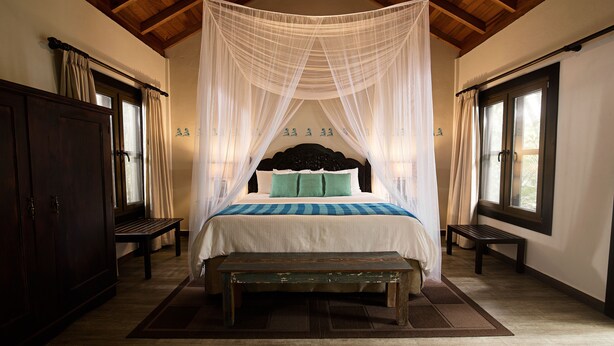 A bedroom with a canopy bed, wooden floor, and a bench. - Jungle Lodge Hotel (Flores)