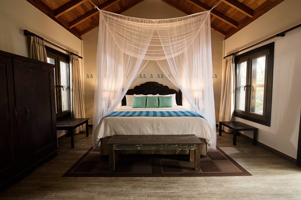A bedroom with a canopy bed, wooden floor, and a bench.