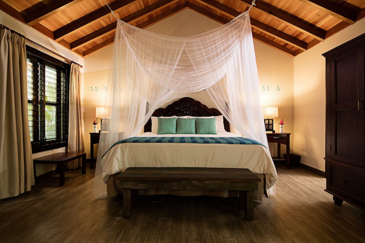 A bedroom with a canopy bed, wooden flooring, a bench, bedside tables with lamps, and a wardrobe.