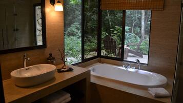 Un baño moderno con un lavamanos grande, una bañera y un ventanal con vistas a una zona boscosa.