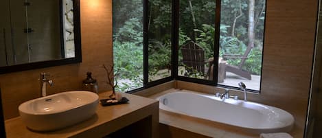 A modern bathroom with a large sink, a bathtub, and a large window offering a view of a forested area.