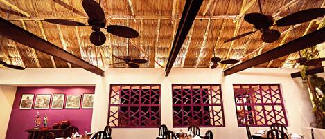 A dining area with a thatched roof, wooden ceiling fans, and traditional decor.