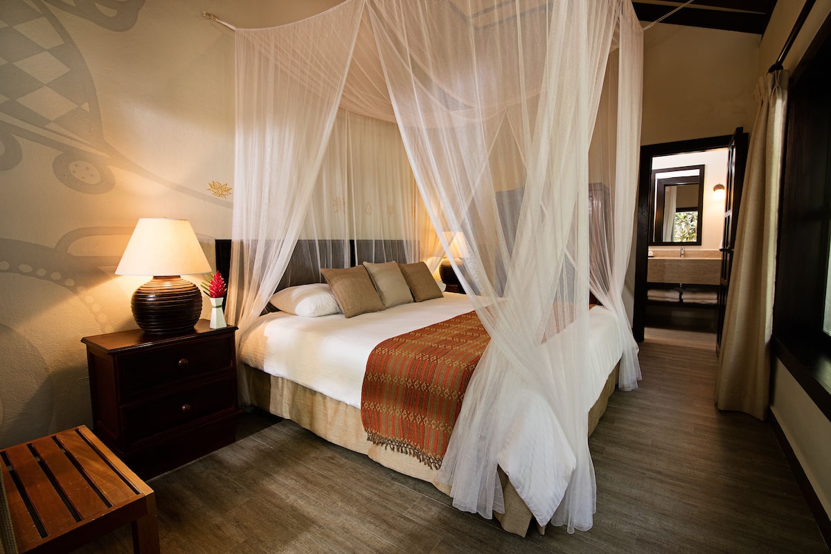 A bedroom with a four-poster bed, a bedside table with a lamp, and a nightstand.