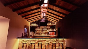 A bar area with wooden beams, a stone wall, and bar stools. - Jungle Lodge Hotel (Flores)