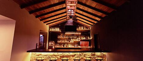 A bar area with wooden beams, a stone wall, and bar stools.