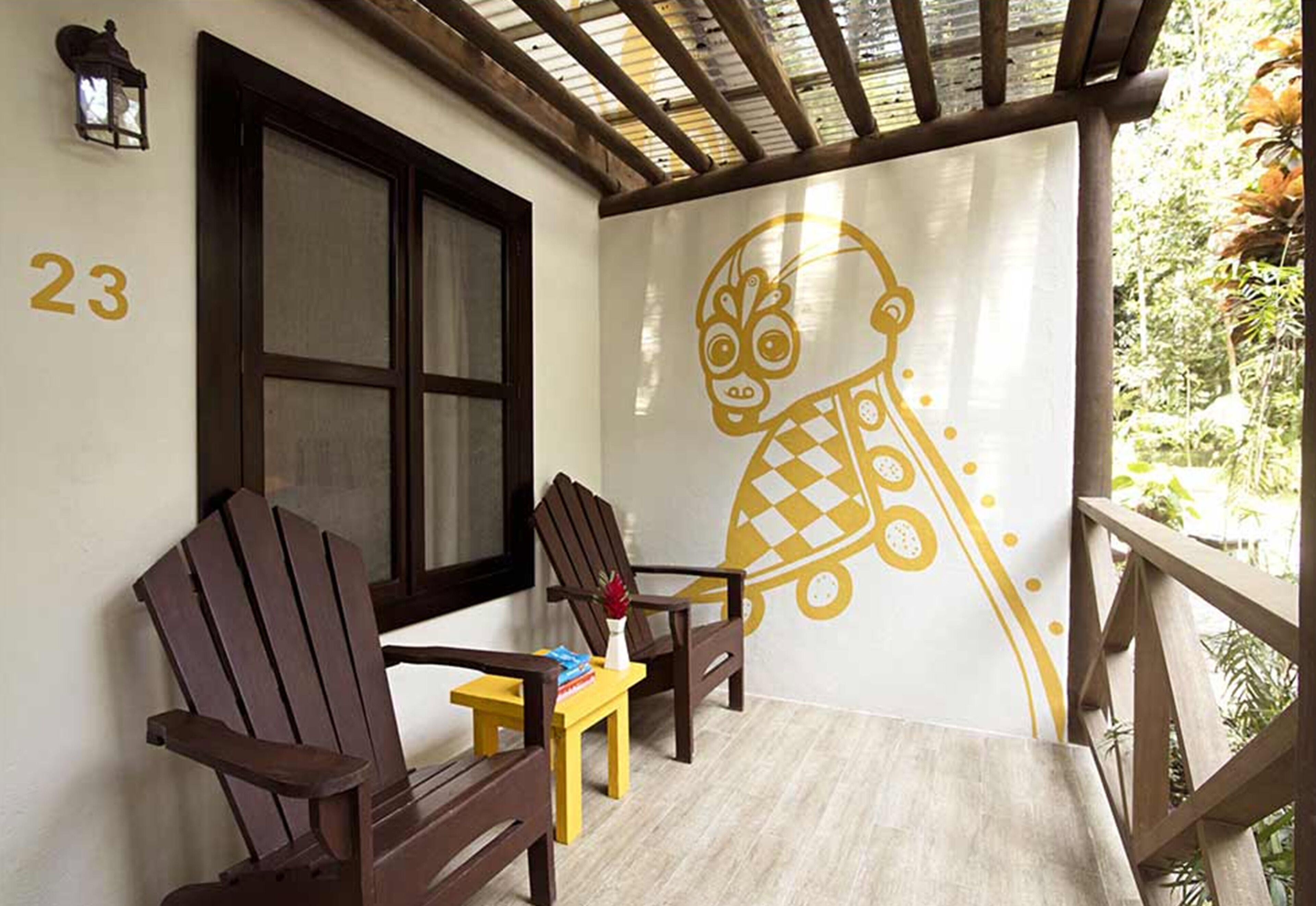 A covered porch with two Adirondack chairs, a small table with a vase, and a wall mural.