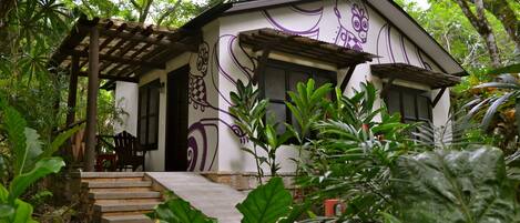 Una casa con porche de madera y escalones que conducen a la entrada, rodeada de exuberante vegetación.