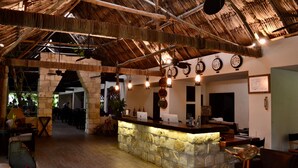 A rustic interior with a stone counter, wooden furniture, and a thatched roof. - Hostal Jungle Lodge Tikal (Flores)