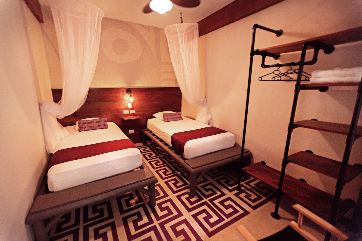 A hotel room with two beds, a bedside table, a hanging clothes rack, and a patterned floor.