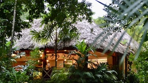 A thatched-roof building surrounded by lush greenery. - Hostal Jungle Lodge Tikal (Flores)